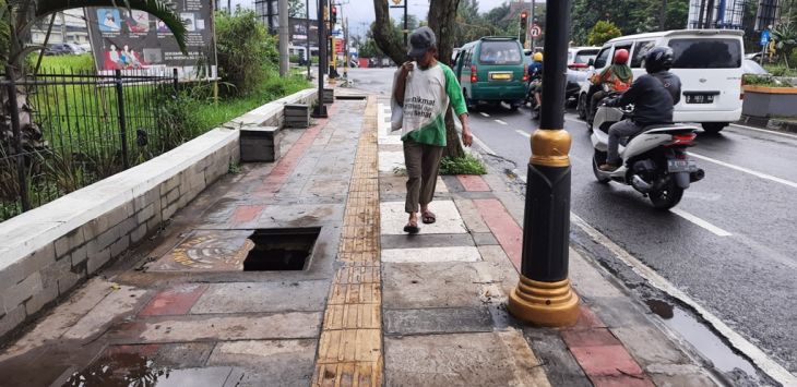 MELINTAS : Seorang warga tengah melintasi lubang bak kontrol yang dibiarkan terbuka di trotoar yang ada di Jalan Raya Soreang.(foto : Fikriya Zulfah/Radar Bandung)