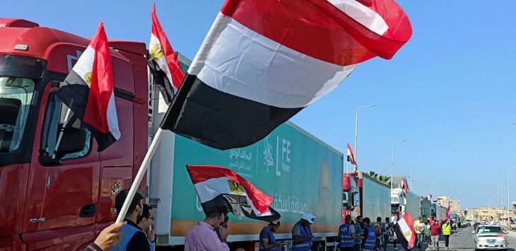 Orang-orang dengan membawa bendera Mesir bersorak-sorak di samping konvoi truk yang membawa bantuan kemanusiaan ke Gaza di kota Al-Arish, Semenanjung Sinai, Mesir. Mereka semua sedang menunggu pembukaan pintu gerbang perbatasan Rafah Gaza-Mesir untuk meny-Stringer-Reuters